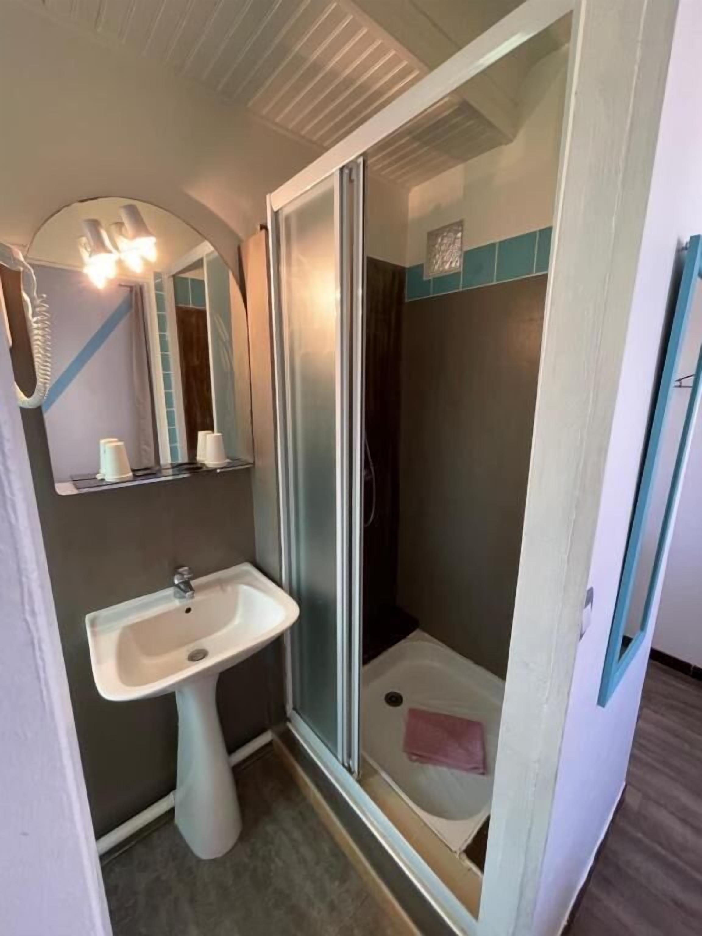 Une petite salle de bain avec un lavabo sur colonne, un espace douche et un miroir.