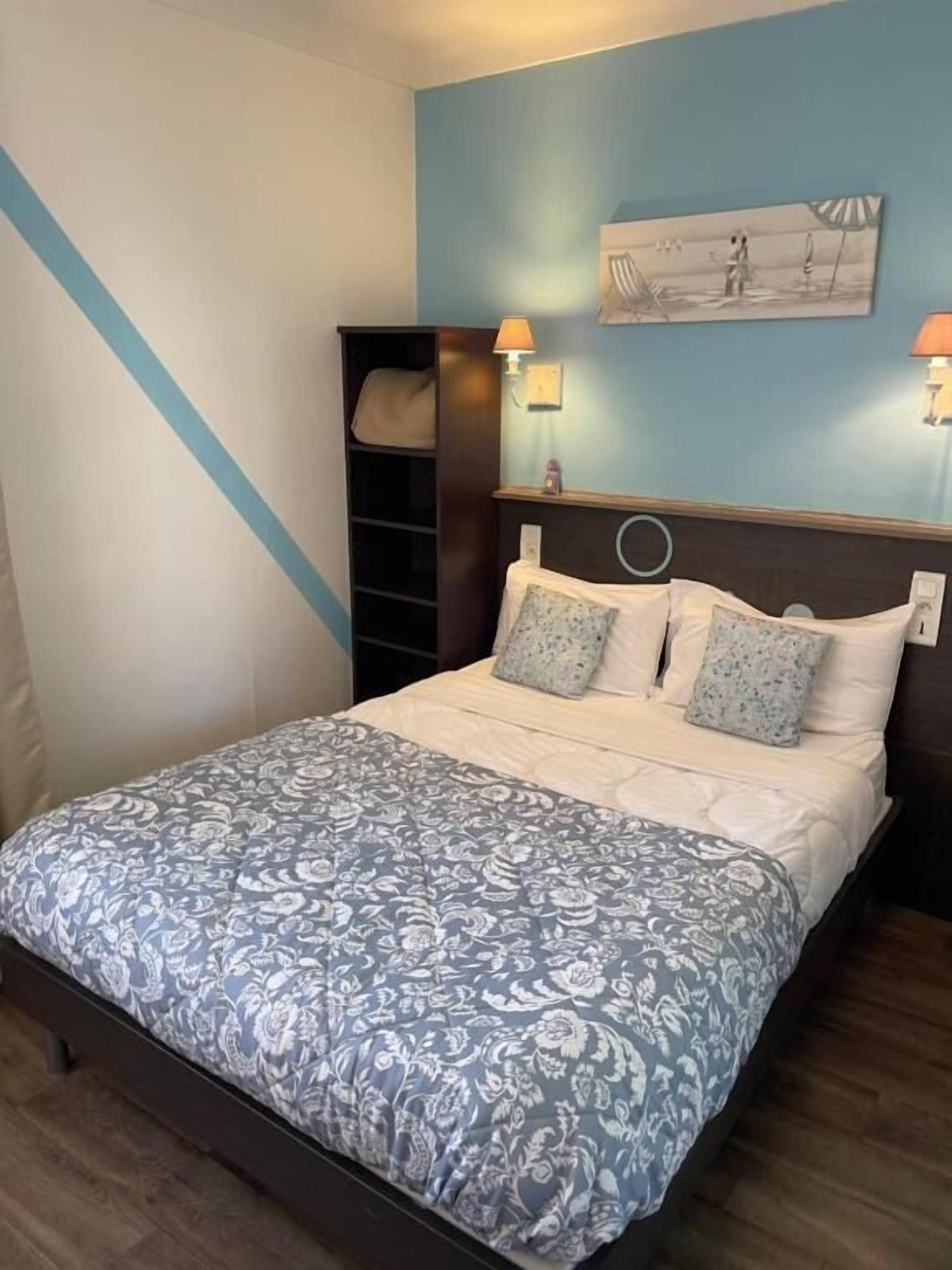 Une chambre à coucher comprenant un lit, une table de chevet, une lampe, un tableau décoratif et une étagère.