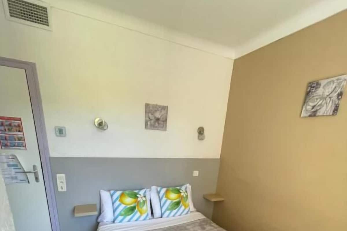 Una cama individual con colchón gris y almohadas estampadas, una mesita de noche pequeña y una lámpara de pared.