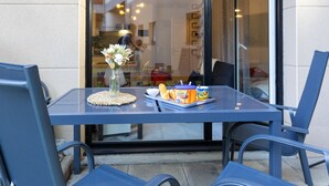 A glass table with chairs, a vase with flowers, and a tray with pastries and a can of drink. - Nautica by Interhome (Saint Malo)