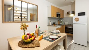 A modern kitchen with a dining table set for two, a refrigerator, and a microwave. - Nautica by Interhome (Saint Malo)