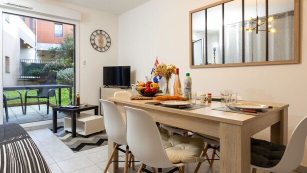 A modern dining area with a wooden table, white chairs, and a large mirror above. - Nautica by Interhome (Saint Malo)