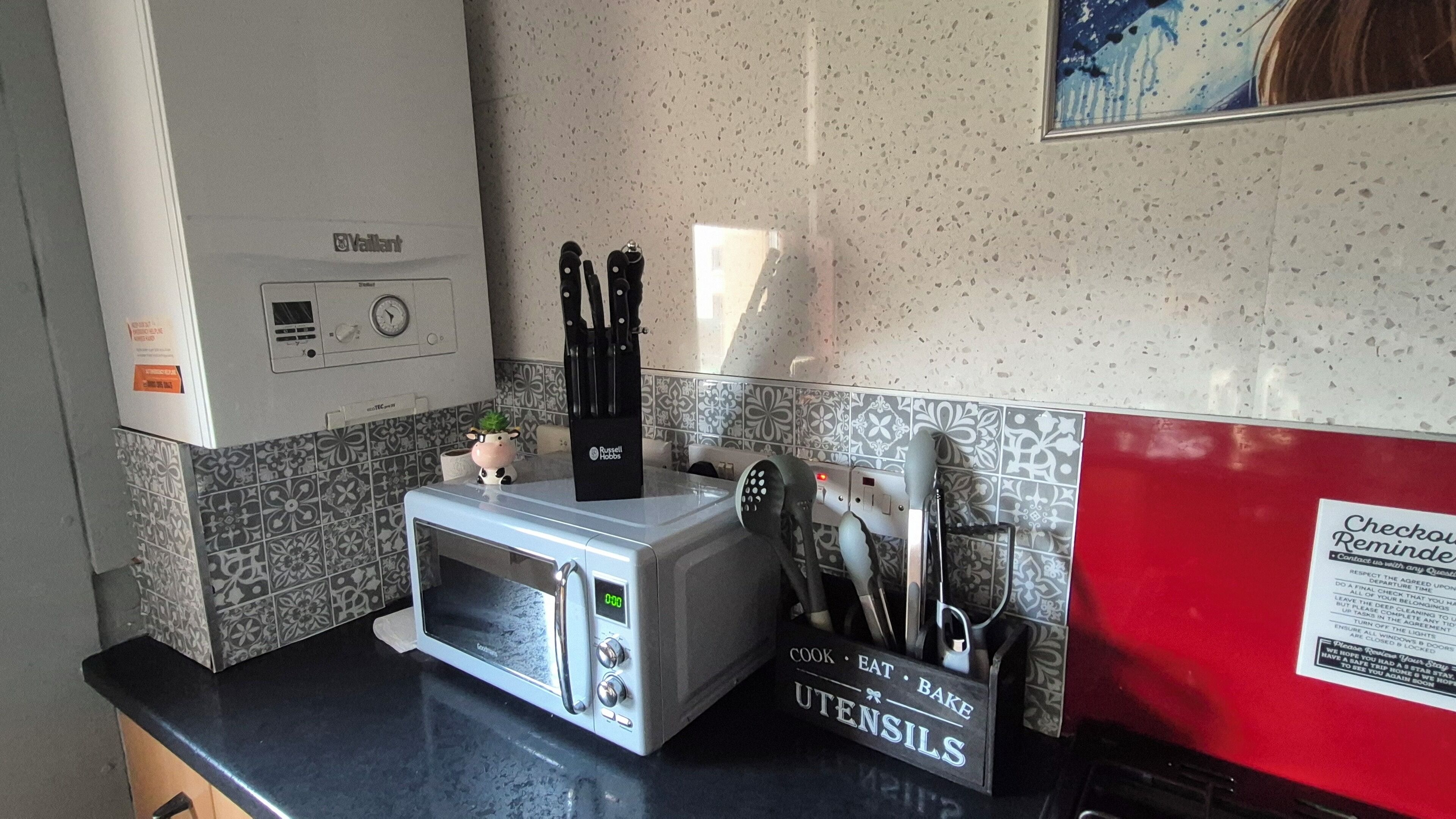 A kitchenette with a microwave, a toaster, and a coffee maker. There is a sign on the wall that reads "Utensils."