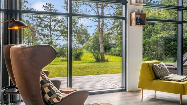 A modern interior with large windows, a brown leather chair, a yellow armchair, and a wooden table.