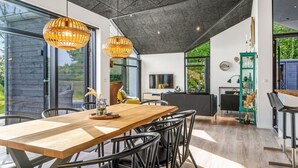 A modern interior with a wooden dining table, black chairs, and a large window offering a view of greenery.