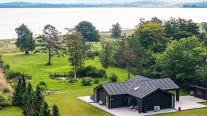 A modern house with a large garage, surrounded by lush greenery and a view of a lake.