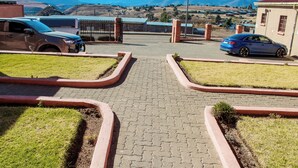 Una strada asfaltata che conduce a un'area parcheggio recintata, con due auto parcheggiate.