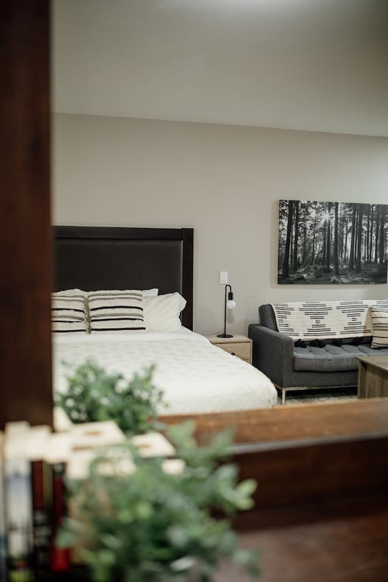 Ein Schlafzimmer mit einem großen Bett, einem Nachttisch mit Lampe, einem grauen Sessel und einem Wandbild.