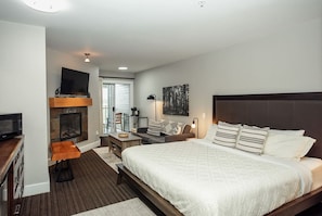 A modern hotel room with a large bed, a flat-screen TV, a fireplace, a desk, and a comfortable seating area. - Forest Stream Escape Suite B (Nanoose Bay)