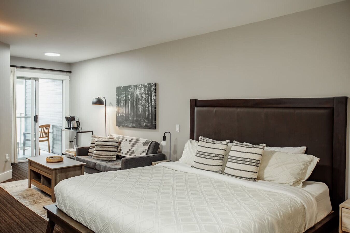 A bedroom with a large bed, a bedside table, a chair, a lamp, and a window with blinds.