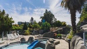 A swimming pool with a slide, lounge chairs, and rocky landscaping. - Escape & Unwind in Suite A (Nanoose Bay)