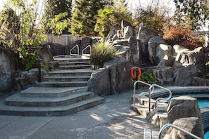 Un espace piscine agrémenté d’un escalier en pierre menant à la piscine, le tout entouré de rochers et de verdure.