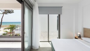 Ett modernt hotellrum med en balkong med utsikt över en strand, en säng med ett träfärgat sänggavel och ett nattduksbord med en lampa.