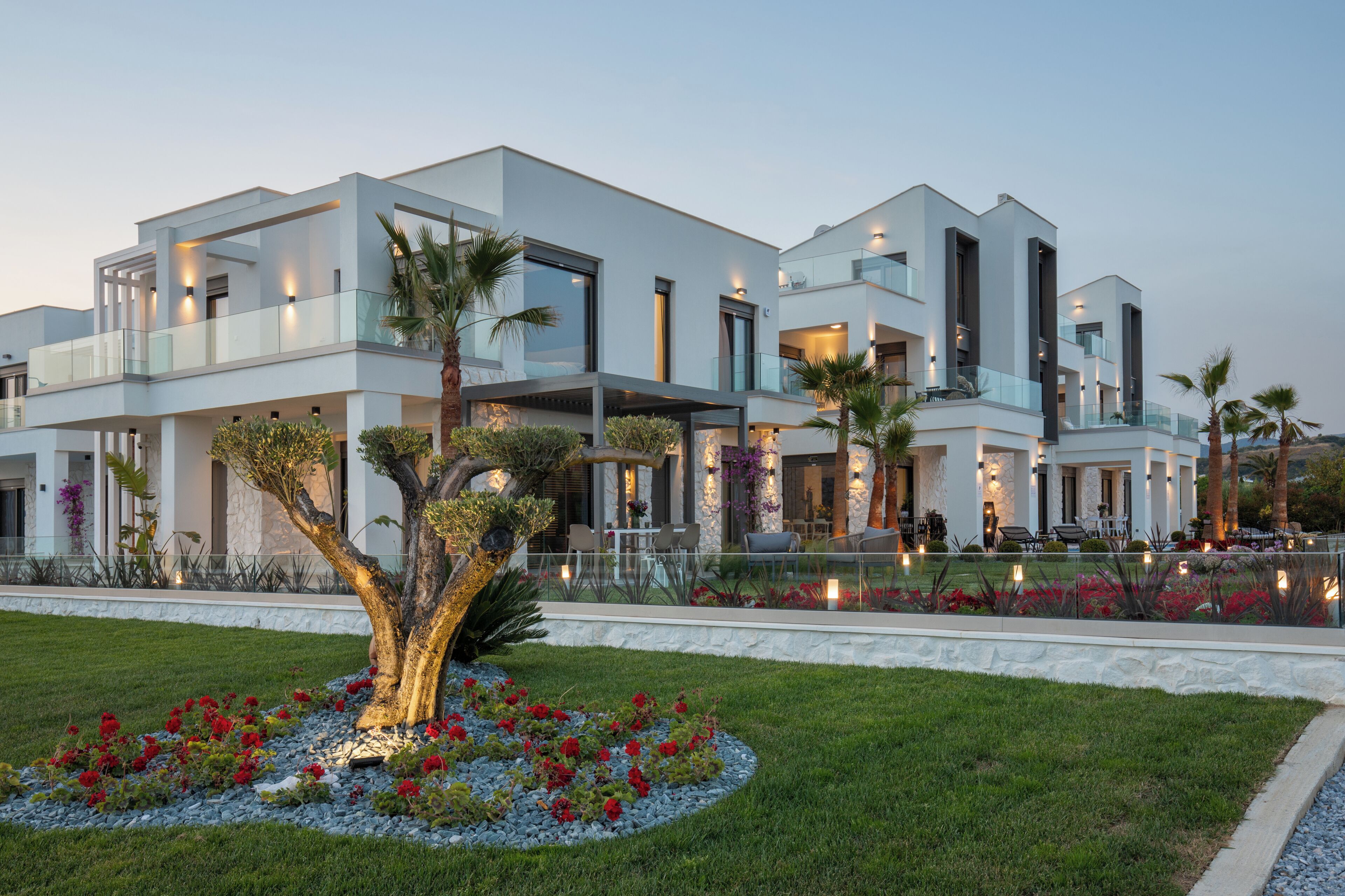 Une maison moderne à plusieurs étages, dotée d’un jardin bien entretenu, d’un espace extérieur aménagé pour se détendre et d’un grand arbre à l’avant.