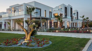 Una casa moderna de varios pisos con un jardín cuidado, un área de estar al aire libre y un gran árbol en la fachada.