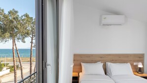 Habitación de hotel con cama, mesita de noche, lámpara, aire acondicionado y vistas al mar y a árboles.