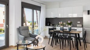 Una cocina moderna con armarios blancos, una zona de comedor con sillas negras y vistas a una piscina exterior.
