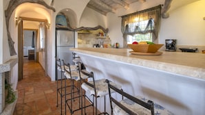 A kitchen with a stone floor, wooden beams, a large island with bar stools, and a refrigerator. - Stazzo Serafini by Interhome (Rena Majore)