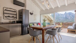 Una cocina moderna con refrigerador empotrado, un comedor con mesa y sillas de madera, y un amplio ventanal con vista a la montaña.