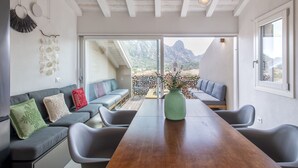 Una sala moderna con una mesa de comedor de madera, sofás grises y vistas a montañas a través de amplios ventanales.