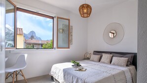 Un dormitorio con cama, escritorio y ventana con vistas a edificios y montañas.