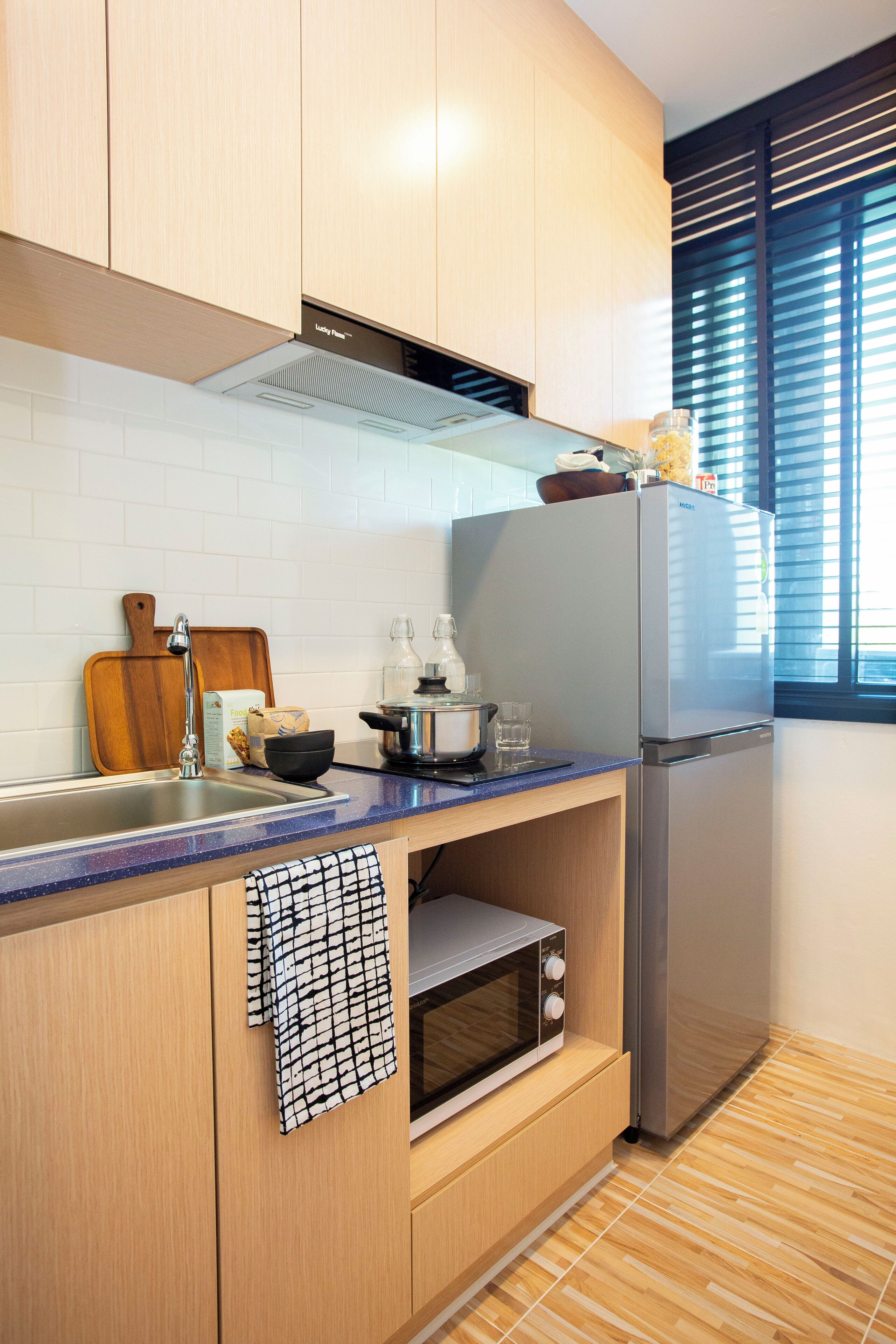 A modern kitchen with wooden cabinets, a stainless steel refrigerator, a built-in oven, and a window with blinds.