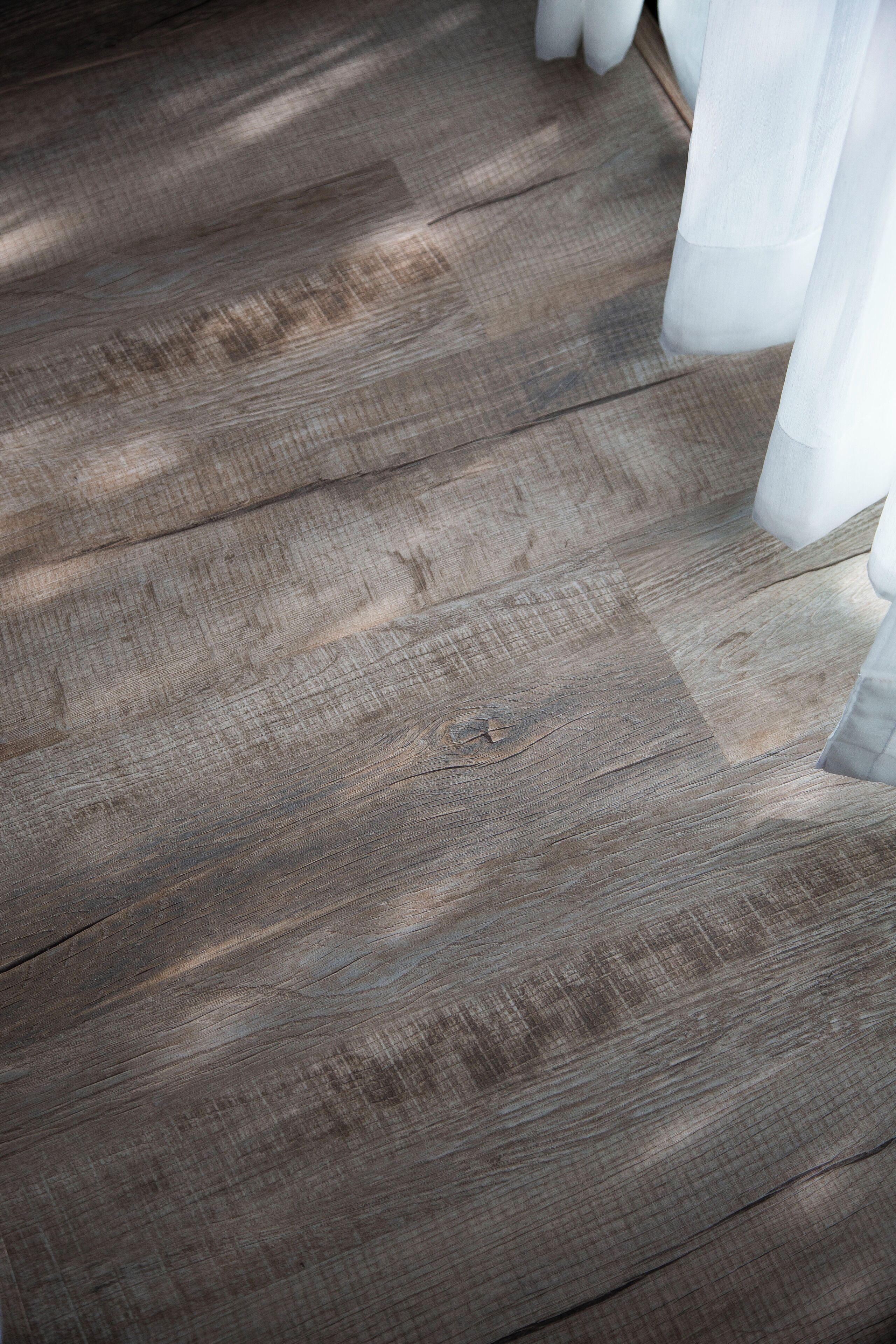 Suelo de madera con acabado natural y una cortina blanca parcialmente visible.
