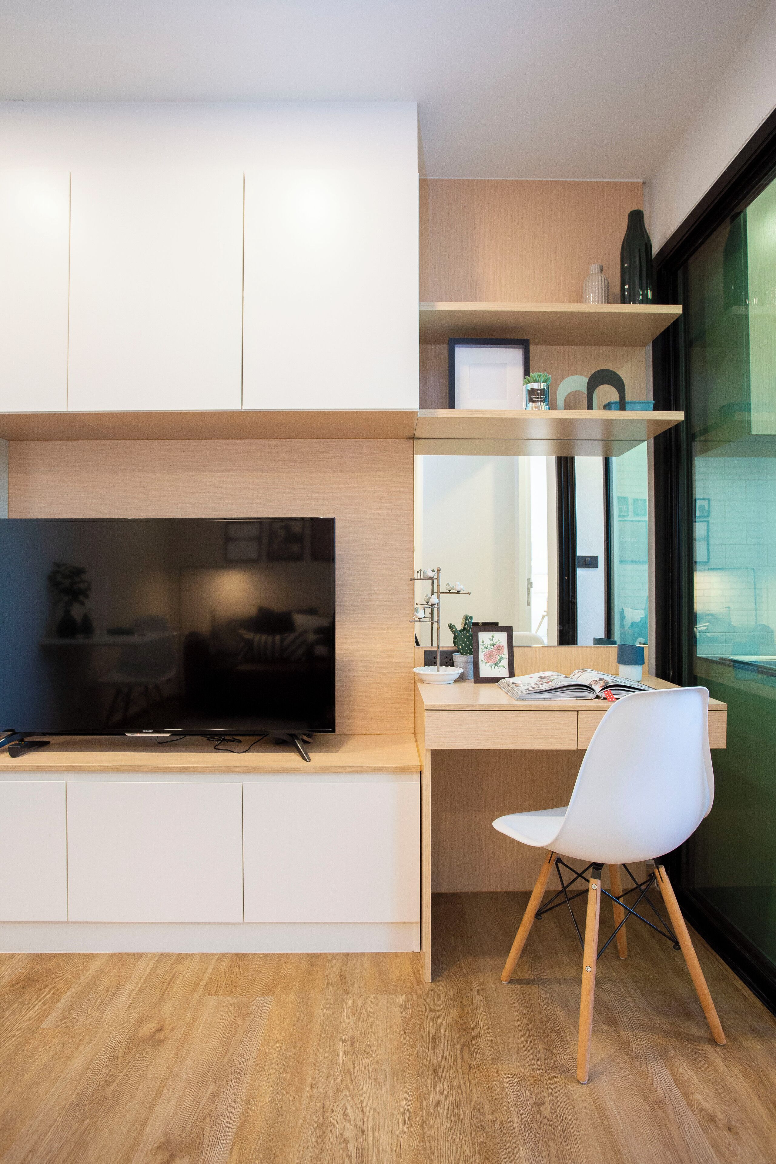 A modern kitchen with a built-in TV, wooden cabinets, a white chair, and a window with a view of the city.