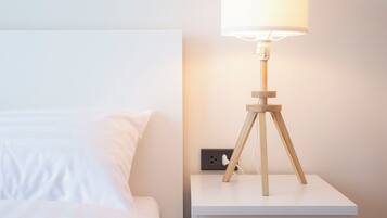 A neatly made bed with white linens, a bedside table with a lamp, and a painting of a blue ocean on the wall.