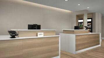 A hotel reception area with a modern design, featuring a reception desk, a digital check-in kiosk, and a visible sign for the Marriott Bonvoy brand.
