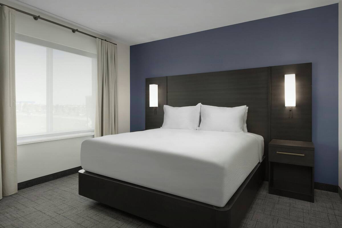 Une chambre d’hôtel moderne avec un grand lit, une table de chevet et une fenêtre avec des rideaux.