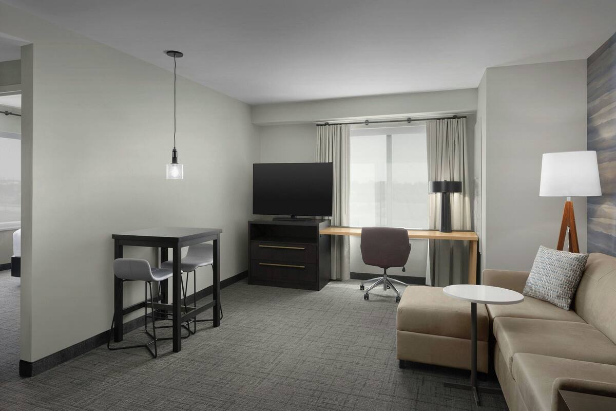Une chambre d’hôtel équipée d’un bureau, de deux chaises, d’une télévision, d’un canapé et d’une lampe.