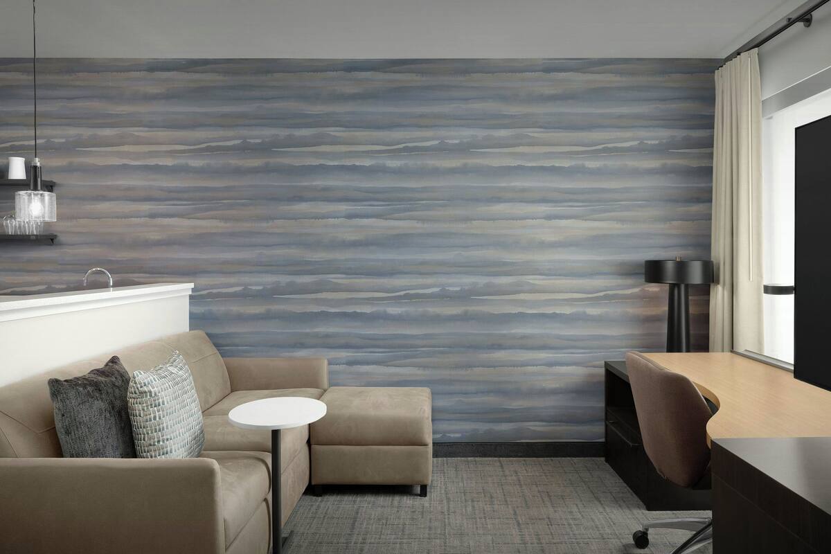 Une pièce moderne avec un mur texturé, un canapé, une petite table ronde, un bureau et une lampe.