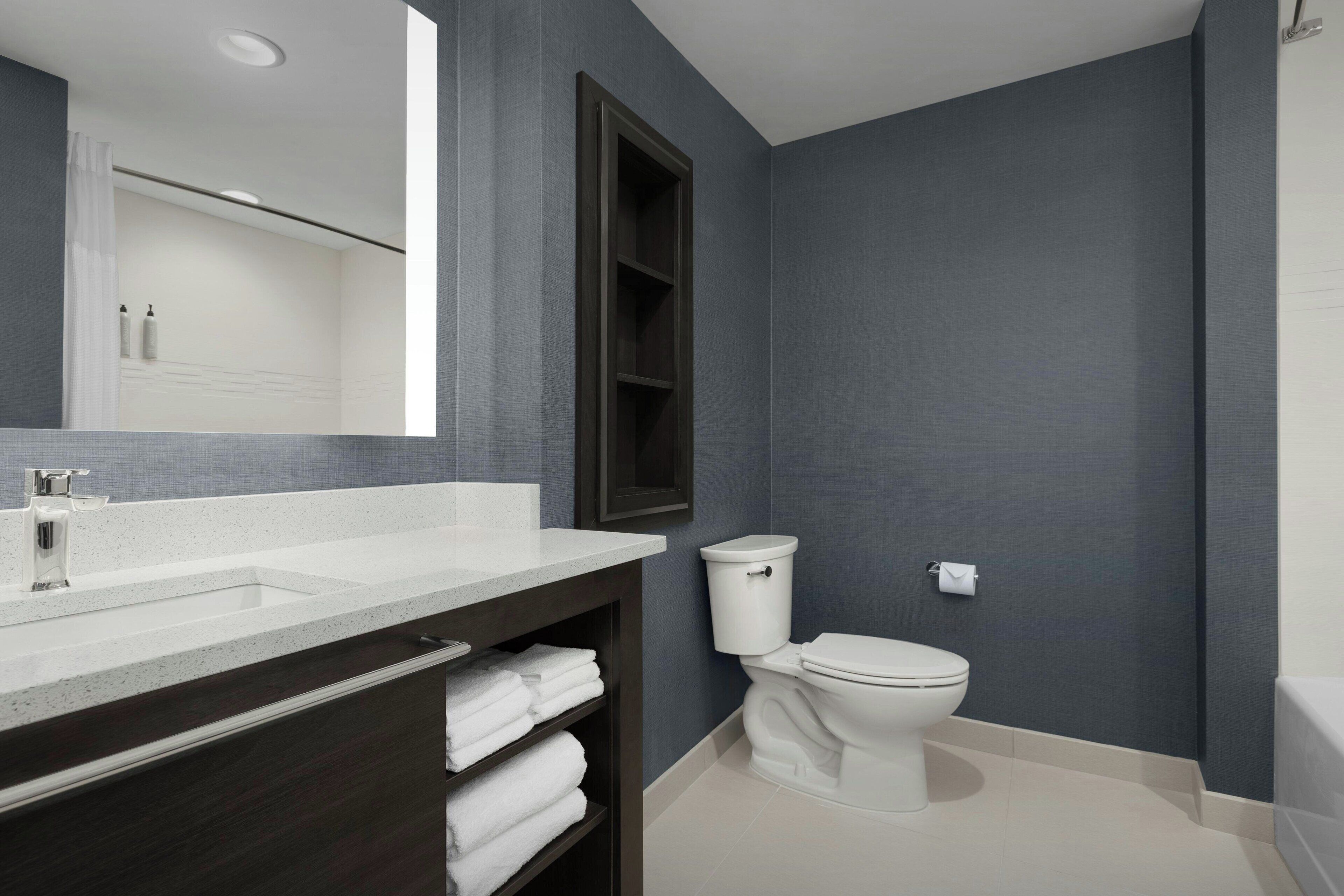 Un baño moderno con un lavamanos blanco, tocador de madera oscura y un inodoro blanco.
