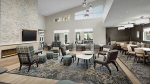 A spacious lounge area with multiple seating options, a flat-screen TV mounted on a stone wall, and large windows providing natural light. - Residence INN BY Marriott Dayton Miamisb (Miamisburg)