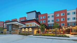 Ein mehrstöckiges Hotel mit modernem Design, das eine Kombination aus roten und grauen Fassaden, großen Fenstern und einem gut beleuchteten Eingangsbereich zeigt.