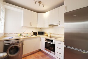 A compact kitchen with white cabinets, a stainless steel refrigerator, a washing machine, and a microwave.