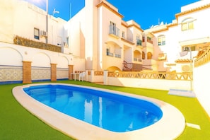 Una piscina con un área verde circundante y edificios blancos con balcones.