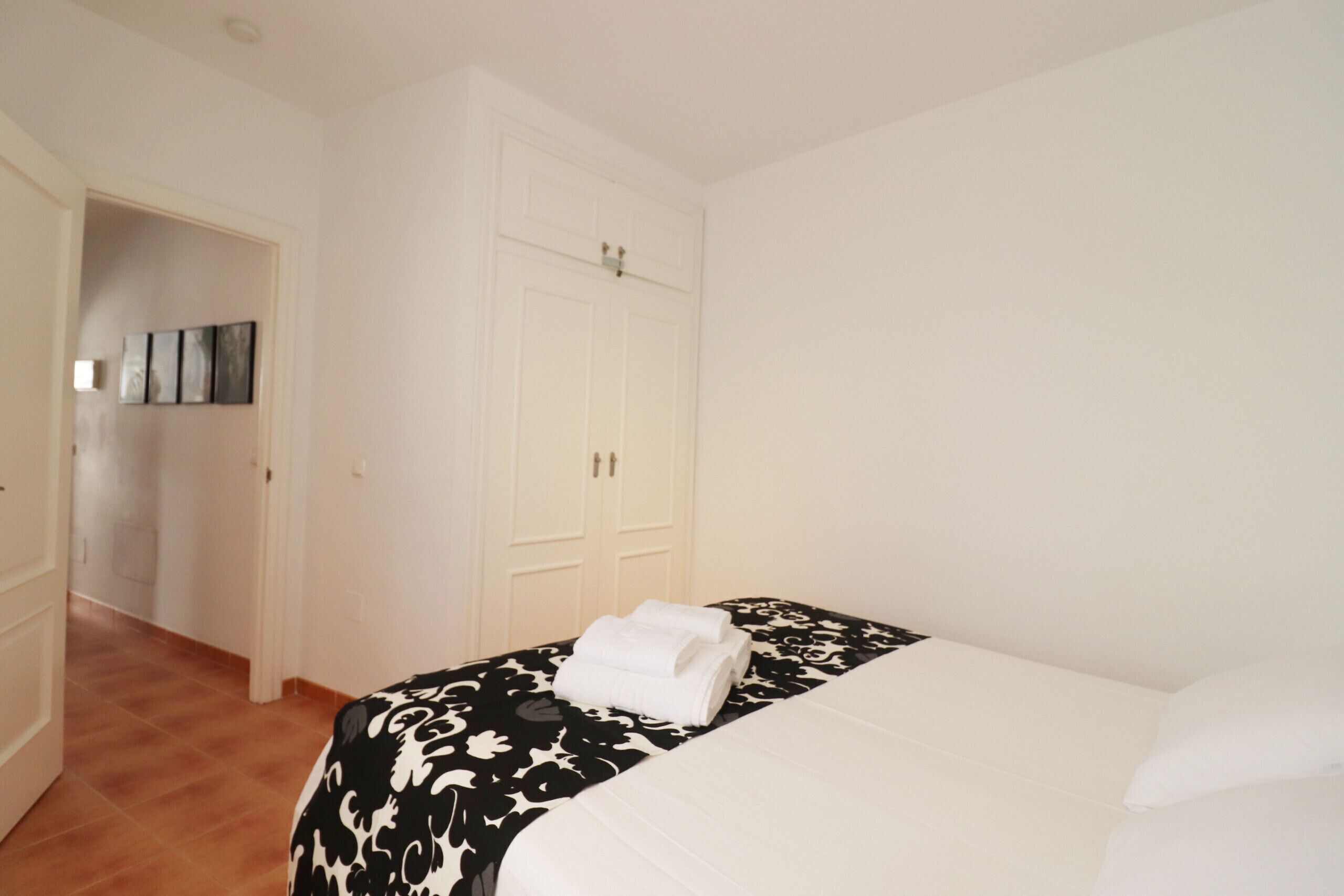 A hotel room with a bed, a wardrobe, and a door leading to another room.