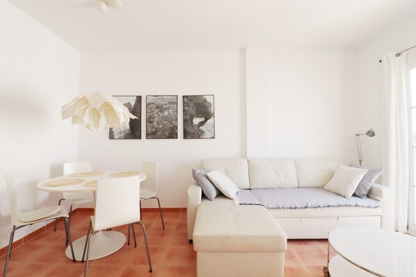 A modern living room with a white sofa, a round dining table with chairs, and three framed pictures on the wall.