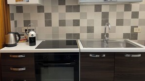 A modern kitchen with a black dishwasher, a stainless steel kettle, a coffee maker, and a microwave. There is a double sink with a faucet, and a large window above the sink. - Melly House: fast Wi-Fi, 5 minutes from the sea (Barletta)