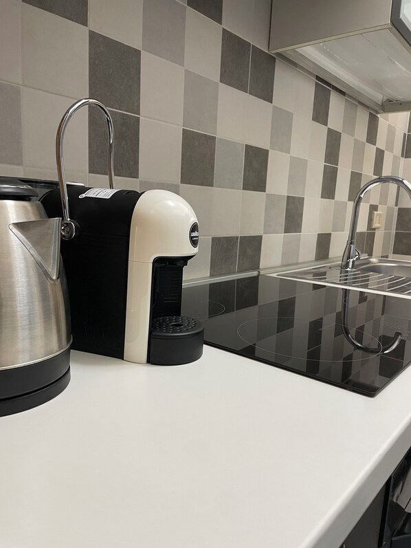 A kitchen with a coffee maker, kettle, and a sink.