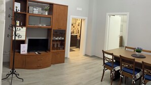 A dining area with a wooden table and chairs, a television on a stand, and a cabinet with glass doors. - Melly House: fast Wi-Fi, 5 minutes from the sea (Barletta)