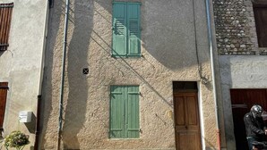 Un edificio de dos plantas con fachada de piedra, contraventanas verdes y una puerta de madera.