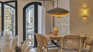 A dining area with a wooden table, wicker chairs, a hanging pendant light, and a decorative vase. - Casa Azalia (Marbella)