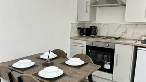A modern kitchen with a dining table set for four, equipped with a stove, oven, and microwave. - Broad Street, Wolverhampton - 2 Bedroom Apartment (Wolverhampton)