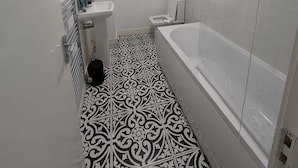 A bathroom with a white sink, toilet, and bathtub. The floor has a black and white patterned tile design. - Broad Street, Wolverhampton - 2 Bedroom Apartment (Wolverhampton)