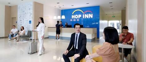 A modern hotel lobby with a reception desk, seating areas, and a luggage trolley.