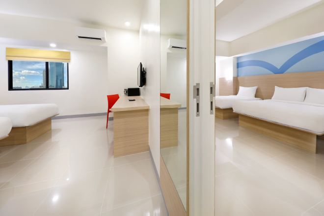 A hotel room with a bed, a desk, a chair, a television, and a window with a city view.