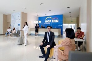 A modern hotel lobby with a reception desk labeled "HOP INN," seating areas, and a map on the wall.